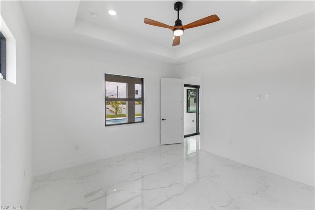 Empty room featuring a ceiling fan, light marble finish flooring, recessed lighting, and a tray ceiling