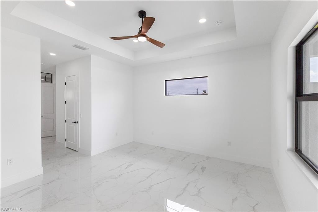 Spare room with healthy amount of natural light, ceiling fan, recessed lighting, a raised ceiling, and light marble finish floors