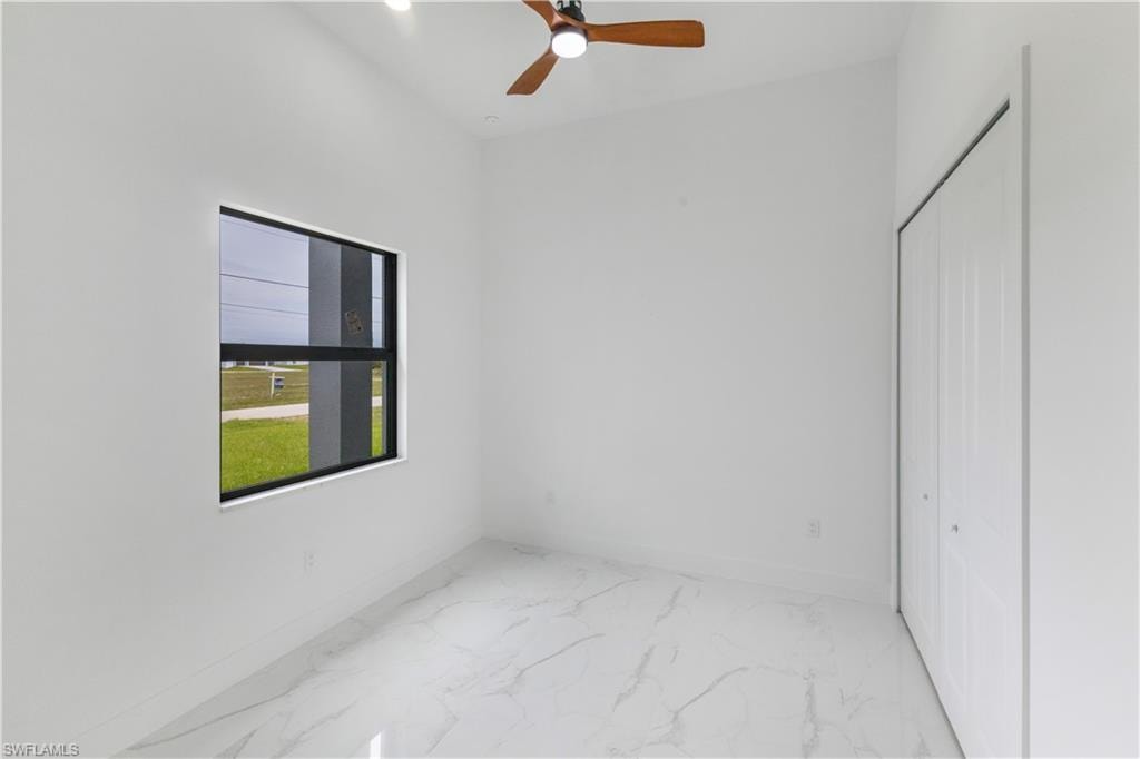 Unfurnished bedroom featuring a ceiling fan, light marble finish floors, and a closet