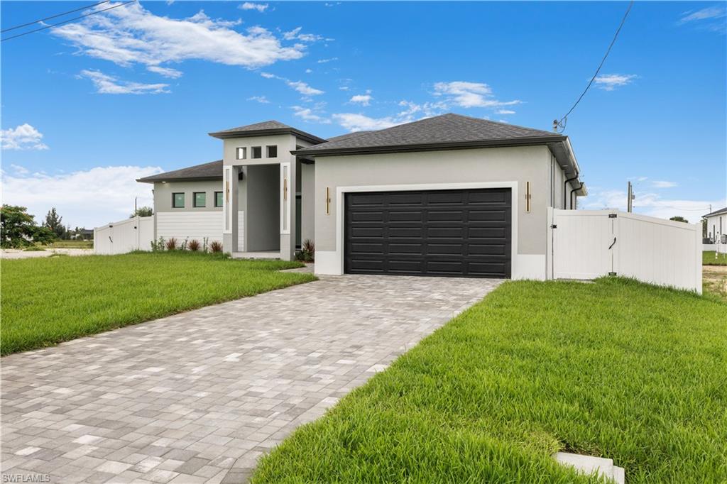 Prairie-style house with a front yard, decorative driveway, stucco siding, an attached garage, and a gate