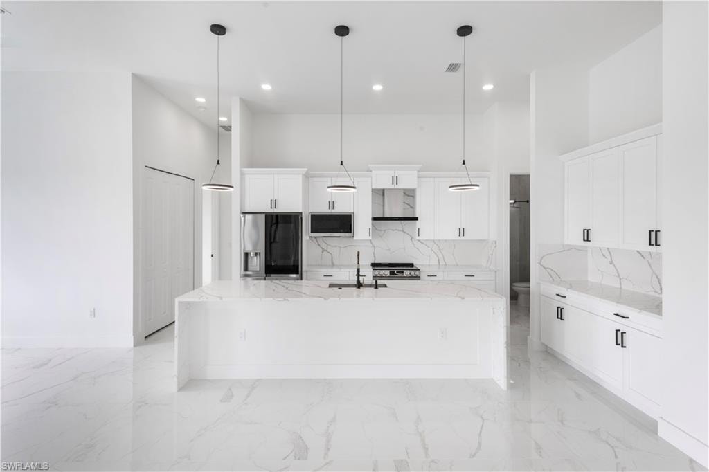 Kitchen with light stone countertops, white cabinetry, a high ceiling, stainless steel appliances, and decorative backsplash