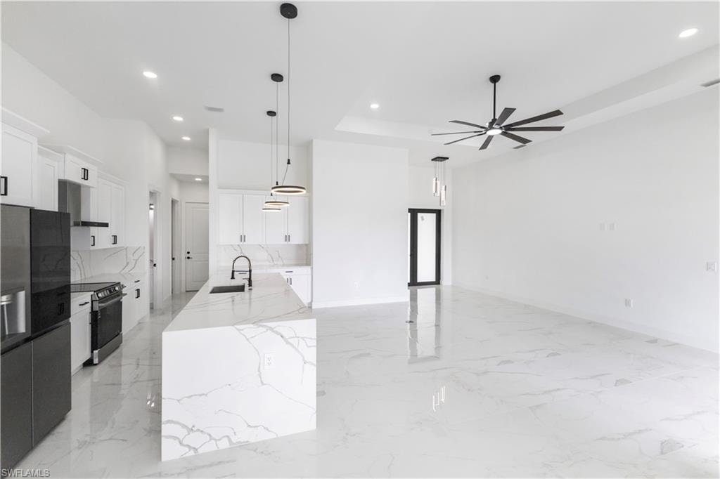 Kitchen featuring white cabinets, stainless steel appliances, light stone countertops, a center island with sink, and decorative light fixtures