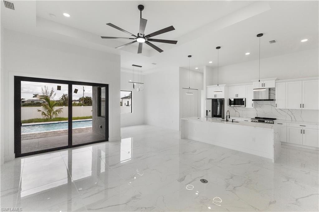 Kitchen with a tray ceiling, white cabinets, light stone countertops, a kitchen island with sink, and stainless steel appliances