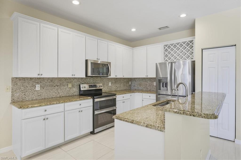 Kitchen with stainless steel appliances, white cabinetry, backsplash, light stone countertops, and recessed lighting