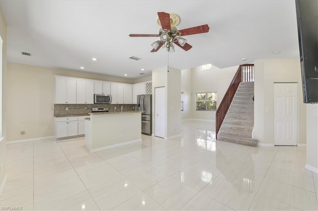 Kitchen with open floor plan, ceiling fan, a kitchen island with sink, white cabinetry, and stainless steel appliances