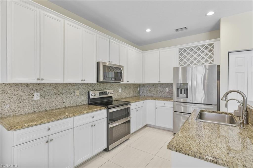 Kitchen featuring stainless steel appliances, white cabinetry, light stone countertops, and recessed lighting