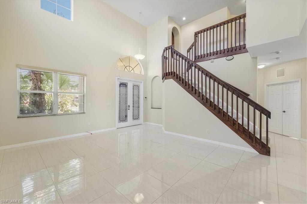 Unfurnished living room with french doors, a high ceiling, light tile patterned flooring, and arched walkways
