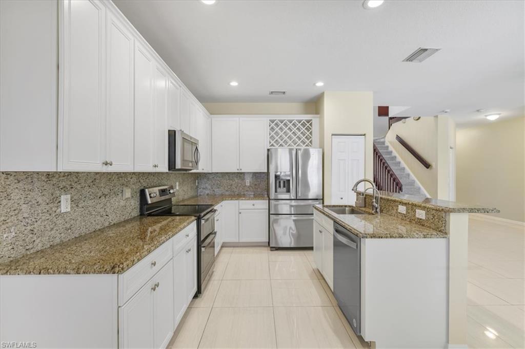 Kitchen with stainless steel appliances, dark stone counters, white cabinetry, a kitchen island with sink, and light tile patterned flooring