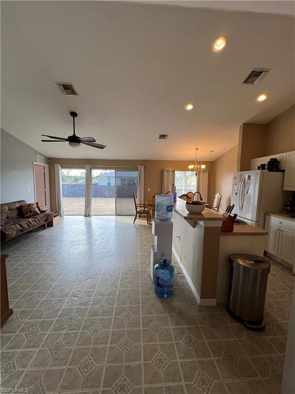 Kitchen with a kitchen bar, a kitchen island, white cabinetry, hanging lights, and a ceiling fan