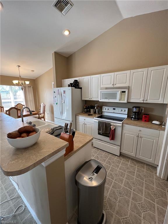 Kitchen with white appliances, white cabinets, a center island with sink, light countertops, and lofted ceiling