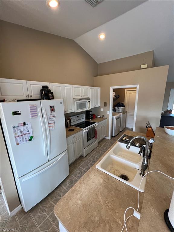 Kitchen featuring white appliances, white cabinetry, lofted ceiling, washer and clothes dryer, and recessed lighting