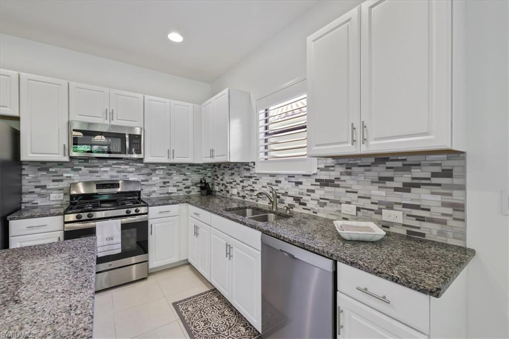 Kitchen with stainless steel appliances, white cabinets, dark stone counters, light tile patterned floors, and recessed lighting