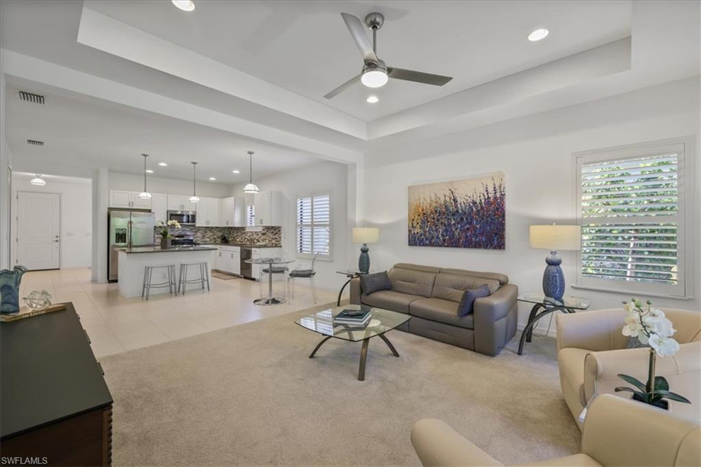 Living area with a tray ceiling, a ceiling fan, light carpet, and recessed lighting