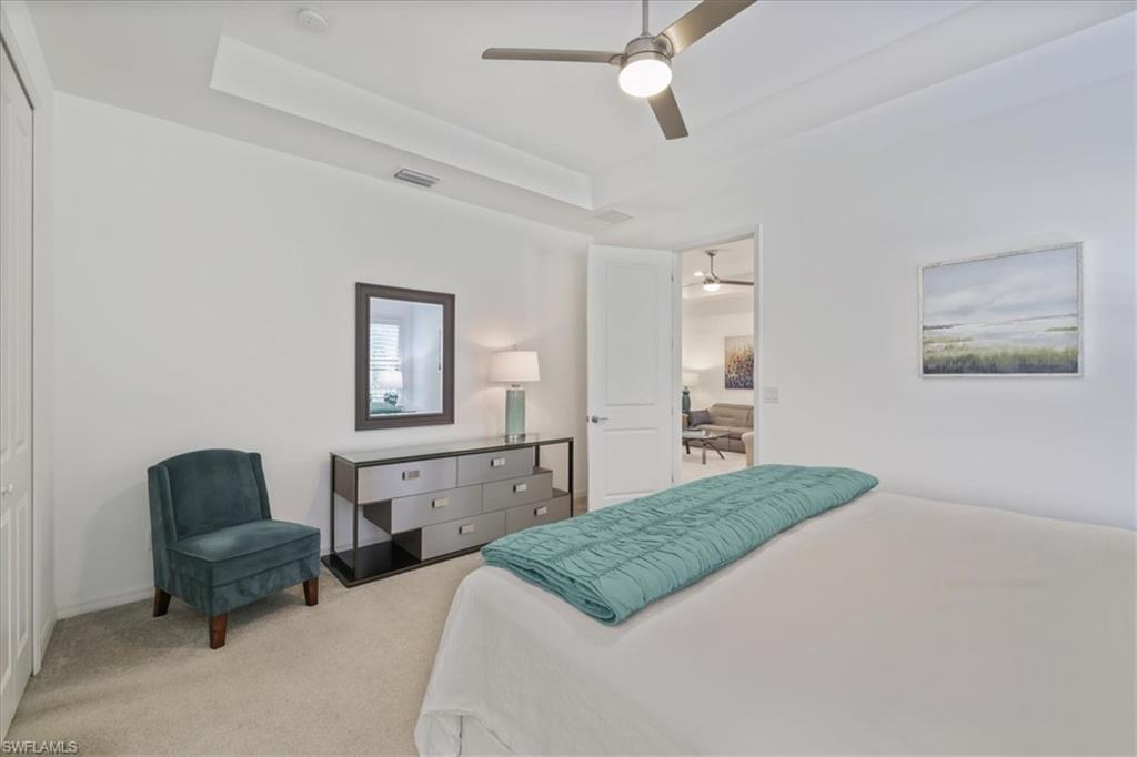 Carpeted bedroom featuring a tray ceiling and a ceiling fan