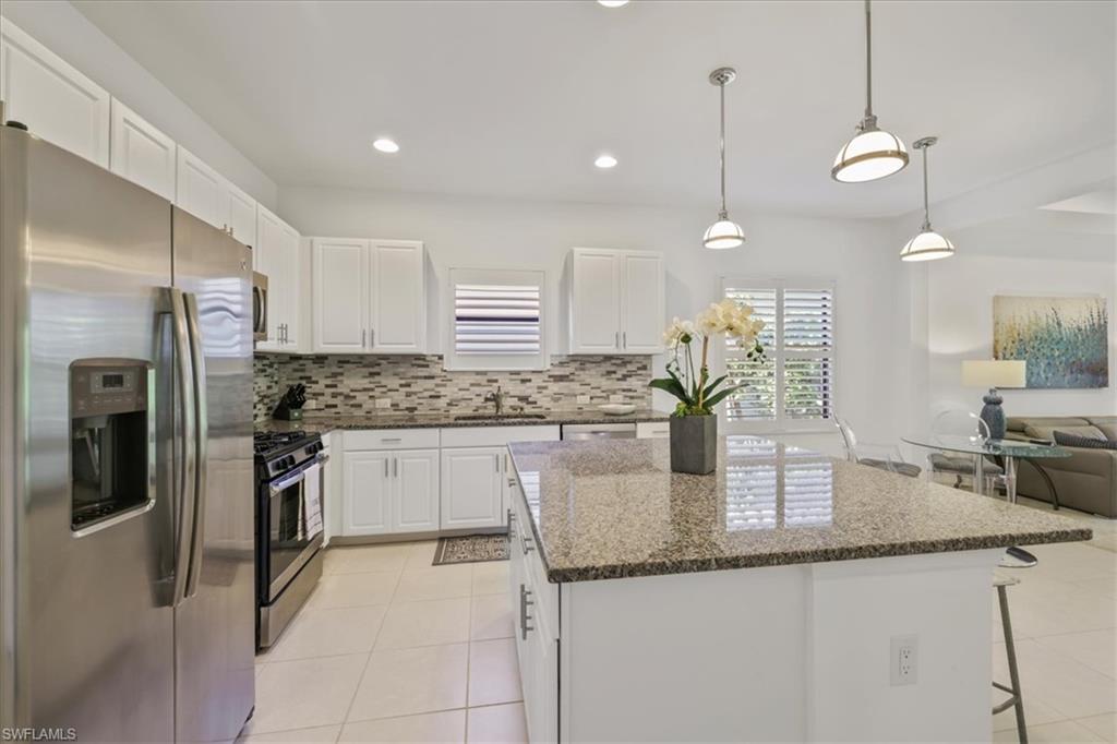 Kitchen featuring stainless steel appliances, a breakfast bar area, hanging light fixtures, white cabinetry, and dark stone countertops