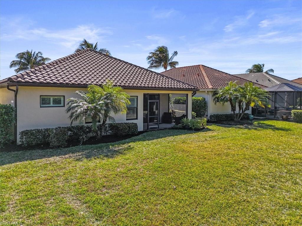 Back of house with stucco siding, a lawn, a sunroom, and a tiled roof