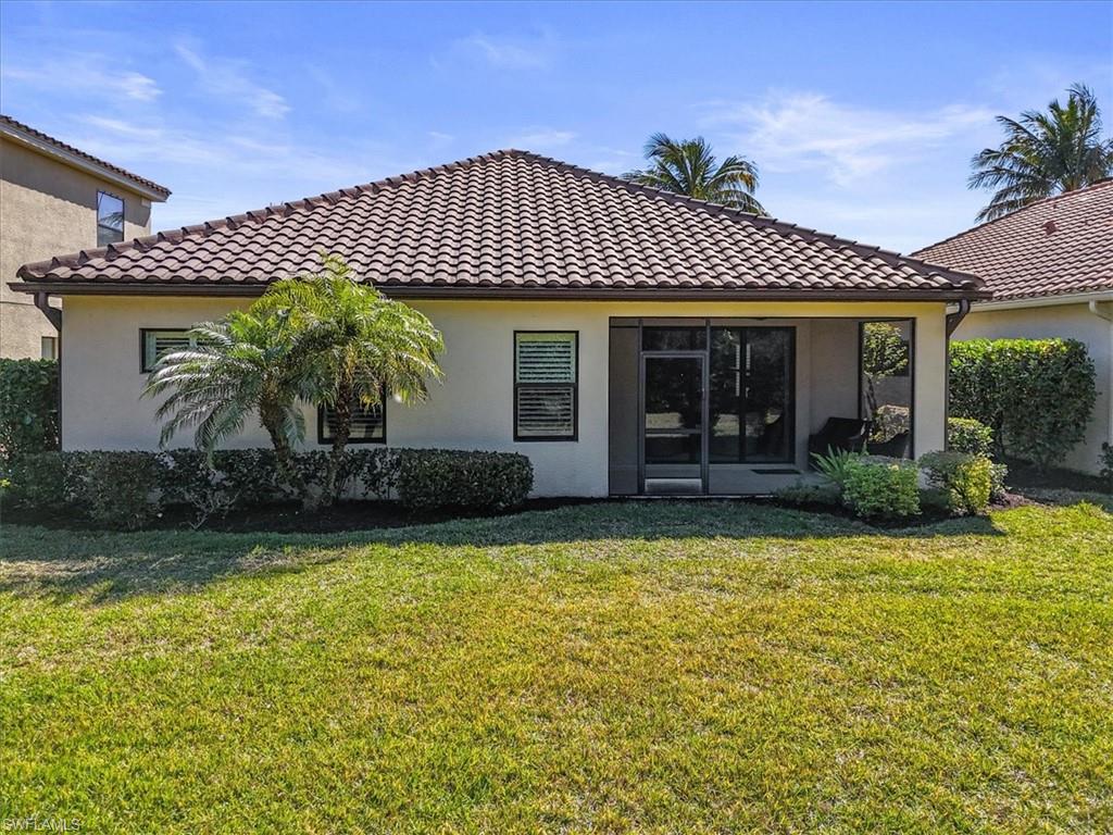 Rear view of house featuring stucco siding, a yard, and a tile roof