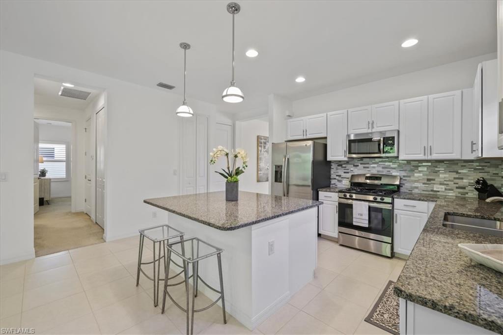 Kitchen featuring stainless steel appliances, a kitchen bar, white cabinetry, dark stone counters, and hanging light fixtures