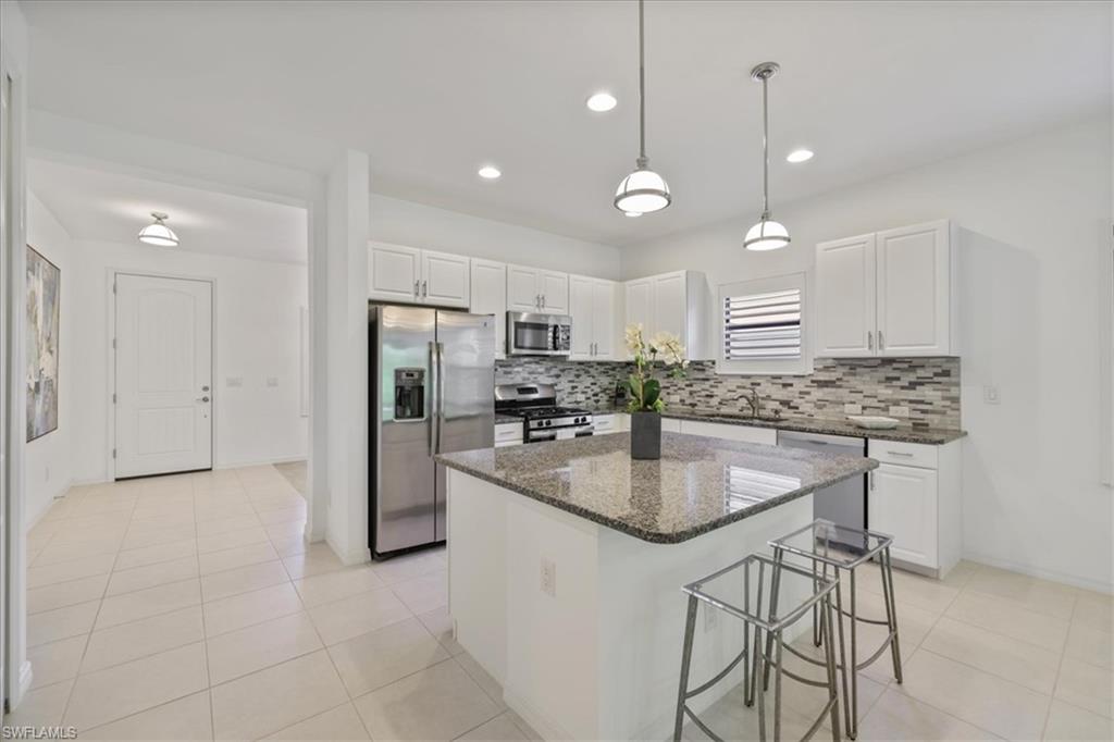 Kitchen featuring a breakfast bar, stainless steel appliances, white cabinets, pendant lighting, and dark stone counters