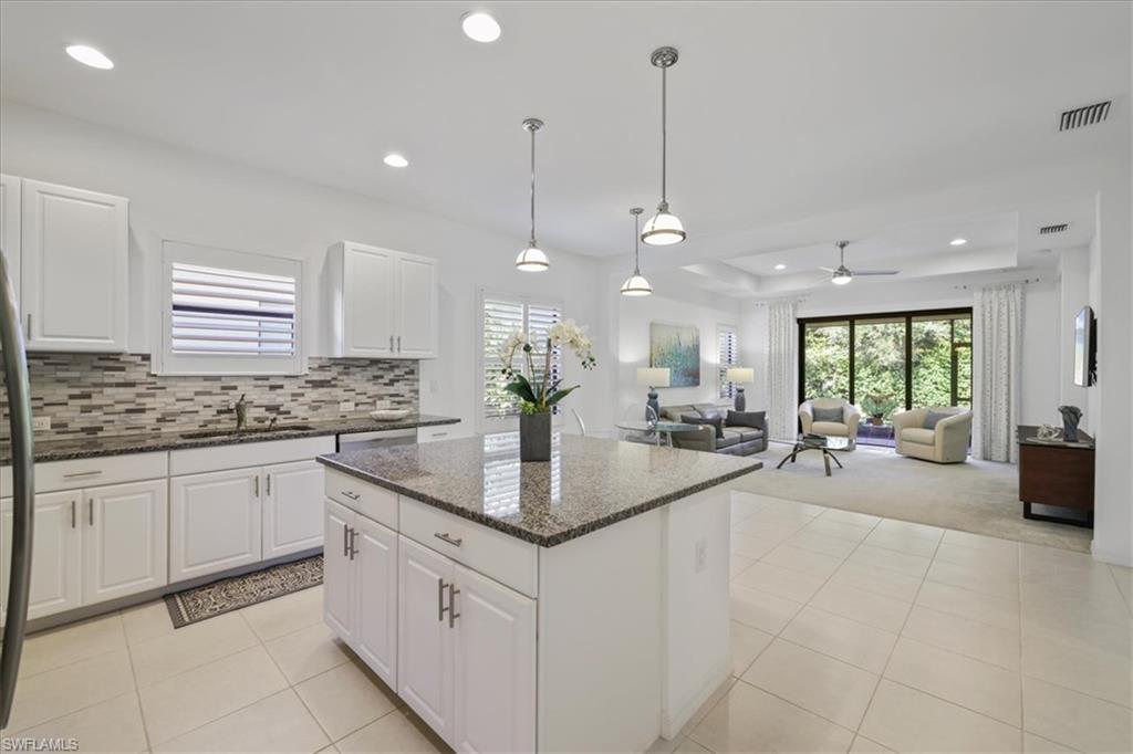 Kitchen with dark stone countertops, decorative light fixtures, white cabinets, a center island, and open floor plan