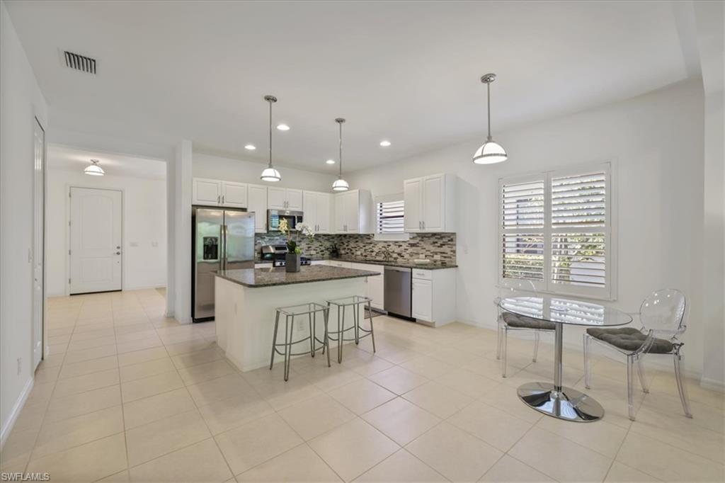 Kitchen with decorative light fixtures, white cabinets, stainless steel appliances, a breakfast bar area, and a kitchen island