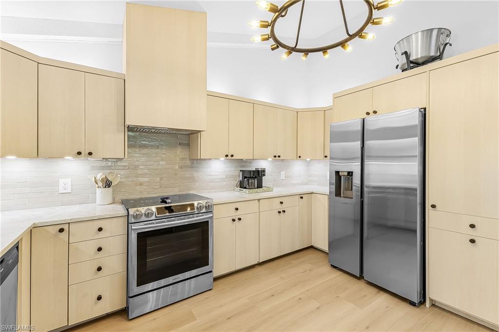 Kitchen featuring stainless steel appliances, tasteful backsplash, Taj Mahal quartz counters, and light wood style flooring & modern  cabinetry