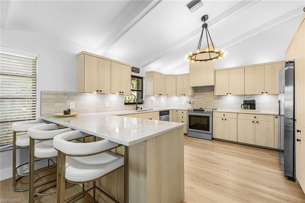 Kitchen with a peninsula bar, light wood style floors, vaulted ceiling with beams, stainless steel appliances, and tasteful backsplash