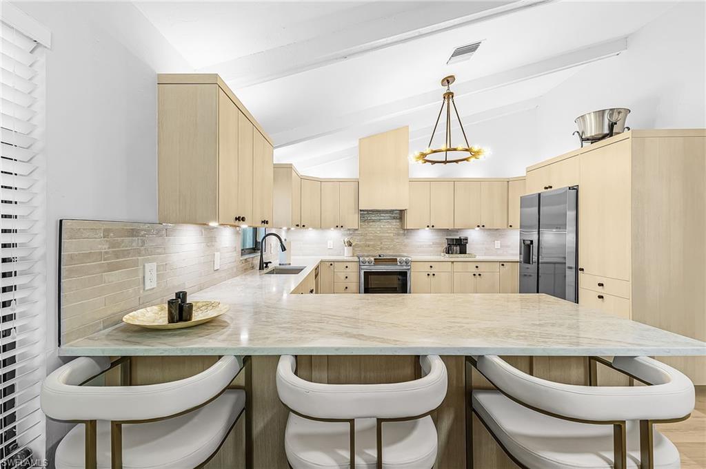 Kitchen featuring a peninsula, light wood finish cabinetry, backsplash, Taj Mahal quartz counters, and vaulted ceiling
