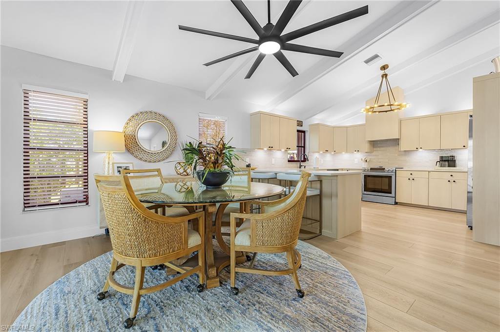 Dining room with vaulted ceiling, beams, light wood-style flooring, a ceiling fan, and a chandelier
