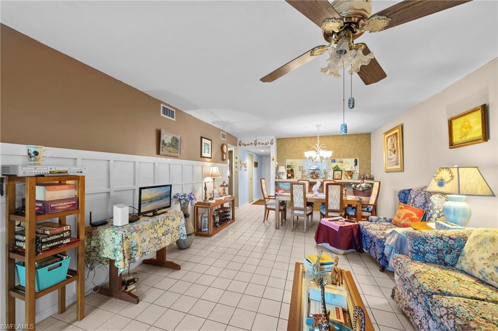 Living room featuring a decorative wall, ceiling fan, light tile patterned flooring, a wainscoted wall, and a chandelier