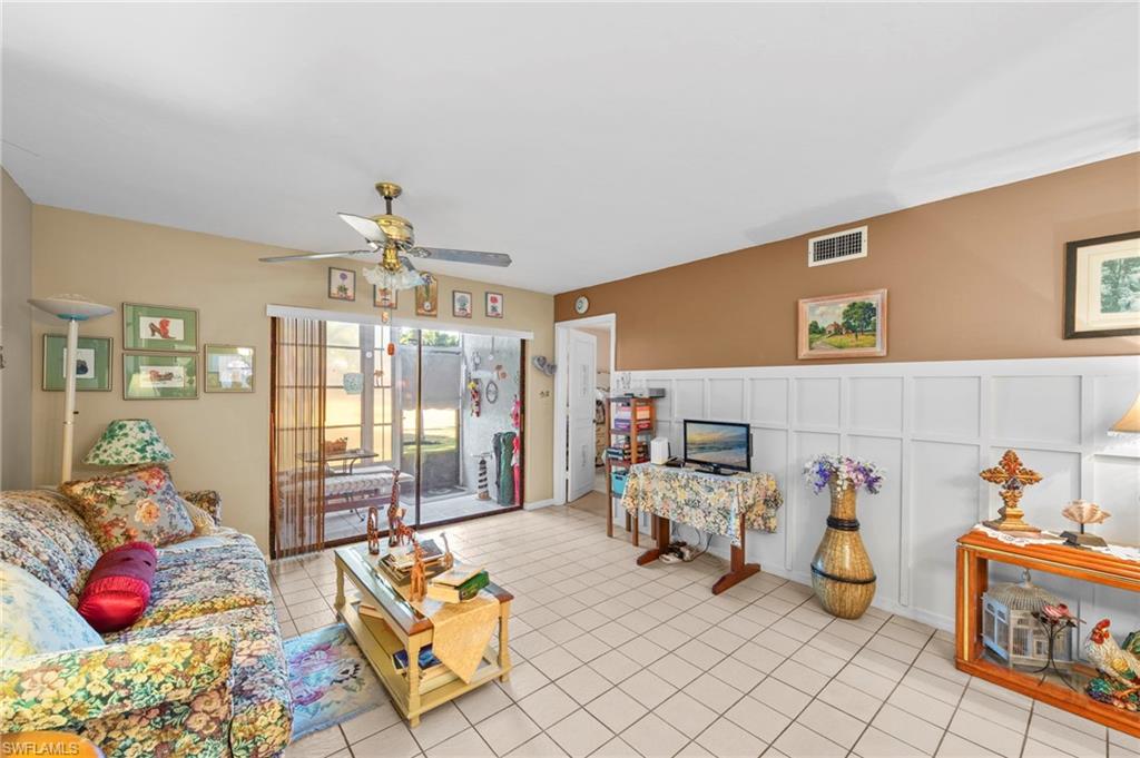 Living area featuring a ceiling fan, a decorative wall, and light tile patterned flooring