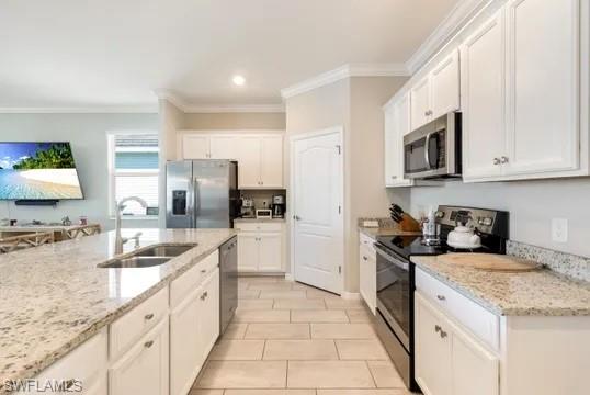 Kitchen featuring stainless steel appliances, white cabinets, crown molding, light stone countertops, and recessed lighting
