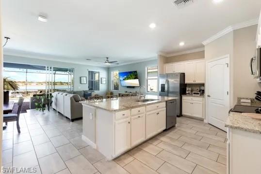Kitchen with white cabinets, light stone counters, open floor plan, a kitchen island with sink, and ornamental molding