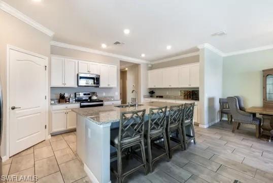 Kitchen with a breakfast bar, white cabinets, stainless steel appliances, a center island with sink, and crown molding