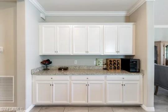 Kitchen featuring white cabinetry, ornamental molding, light stone countertops, and light tile patterned flooring