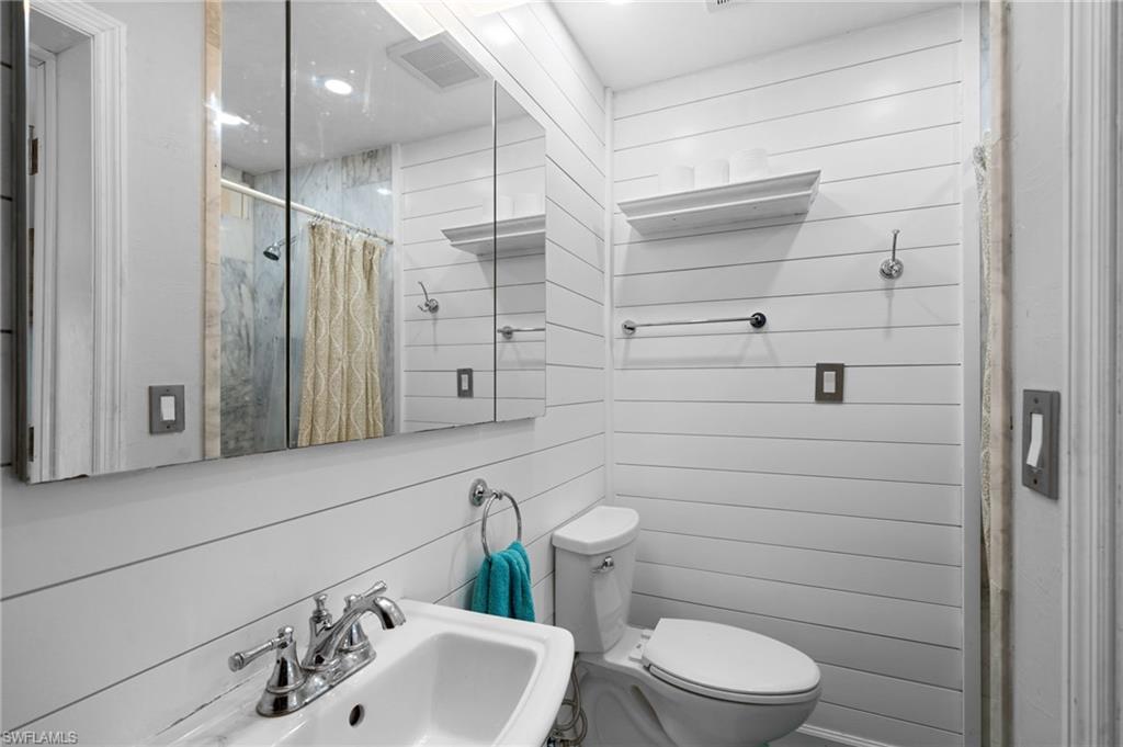 Bathroom featuring wood walls, sink, a shower with shower curtain, and toilet