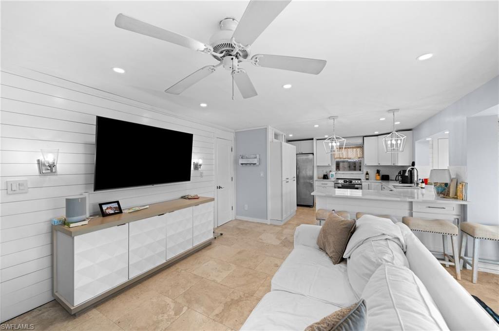 Living room with ceiling fan with notable chandelier, wood walls, and sink