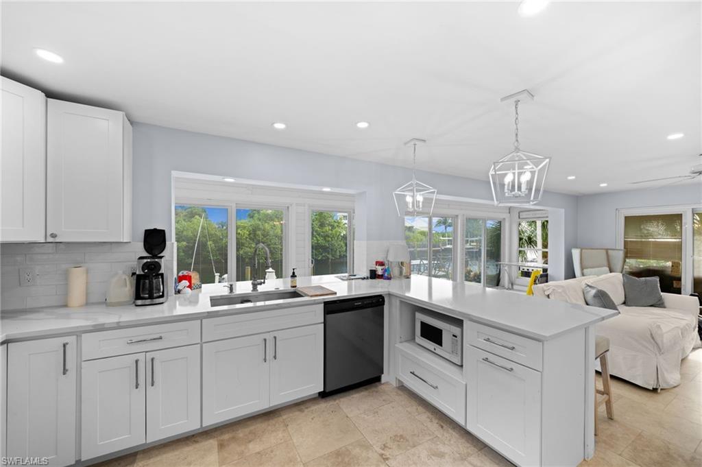 Kitchen with hanging light fixtures, sink, backsplash, white cabinetry, and dishwasher
