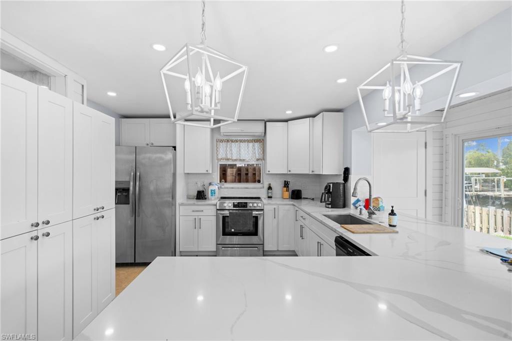Kitchen featuring pendant lighting, light stone counters, stainless steel appliances, and white cabinets