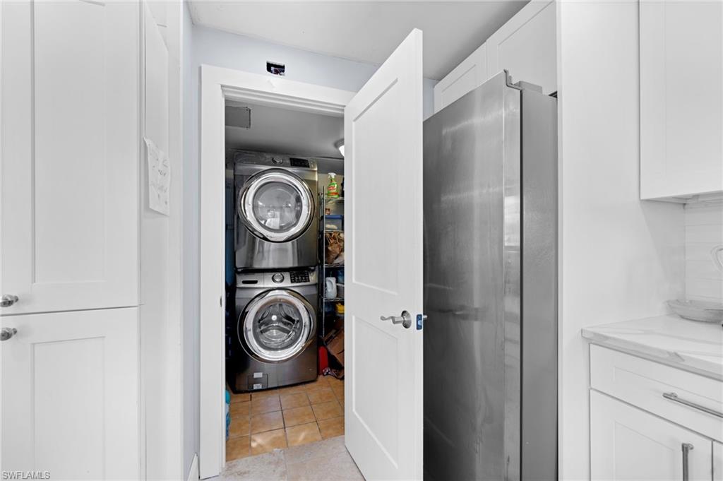 Washroom with stacked washer / drying machine and light tile patterned floors