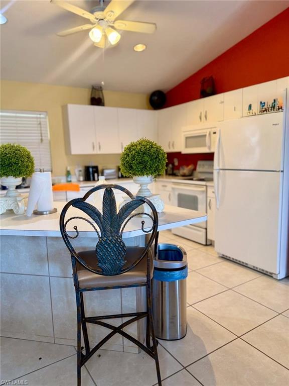 Kitchen with vaulted ceiling, light countertops, white appliances, a ceiling fan, and white cabinets