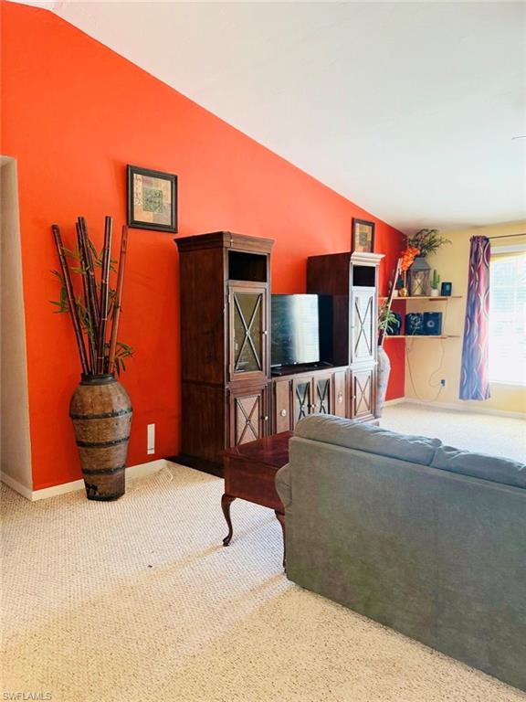 Carpeted living area with lofted ceiling and baseboards