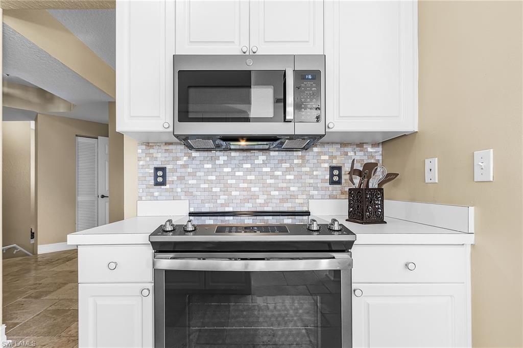 Kitchen with stainless steel appliances, light countertops, white cabinetry, and light stone finish floors