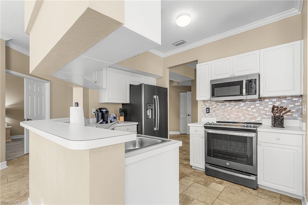 Kitchen featuring ornamental molding, stainless steel appliances, light countertops, a peninsula, and stone tile flooring