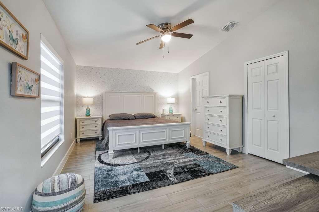 Bedroom with wallpapered walls, a ceiling fan, light wood-type flooring, and lofted ceiling