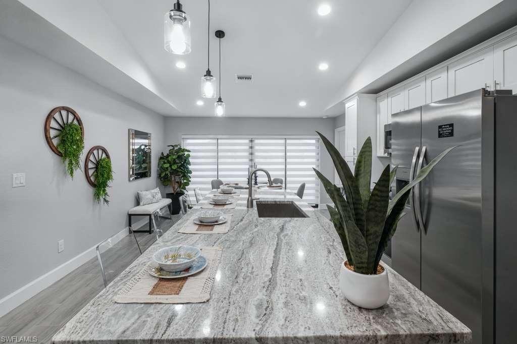 Kitchen with freestanding refrigerator, an island with sink, light stone counters, decorative light fixtures, and white cabinetry