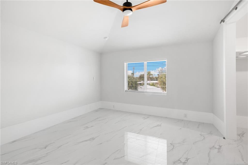 Unfurnished room featuring light marble finish floors, a ceiling fan, and lofted ceiling