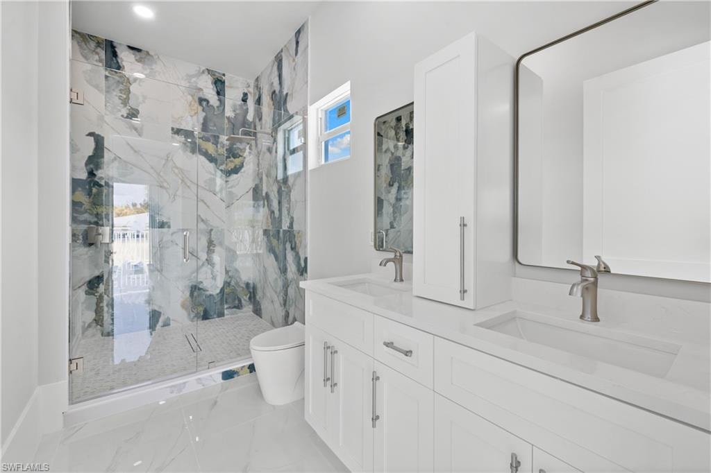Full bathroom featuring double vanity, a marble finish shower, and light marble finish flooring