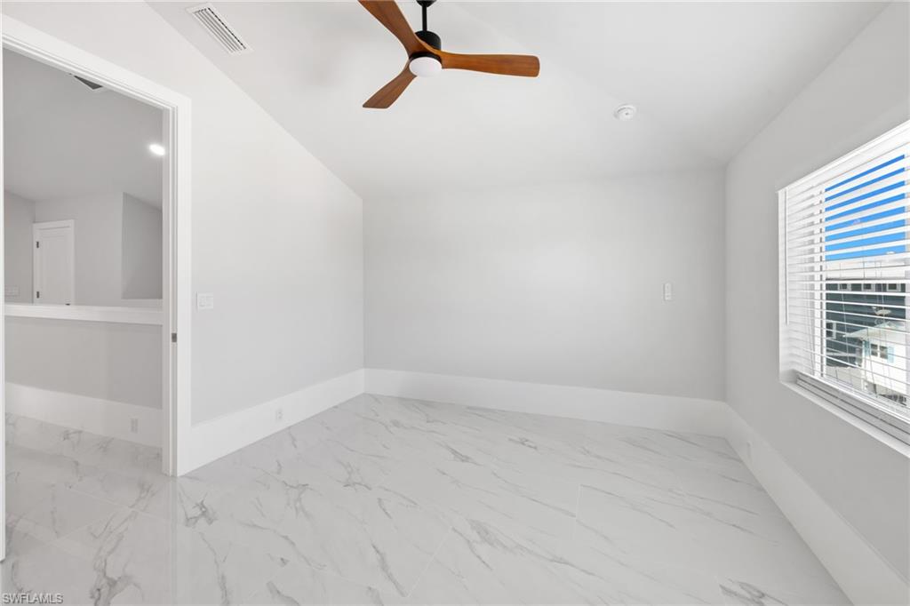 Spare room featuring light marble finish flooring, lofted ceiling, and ceiling fan
