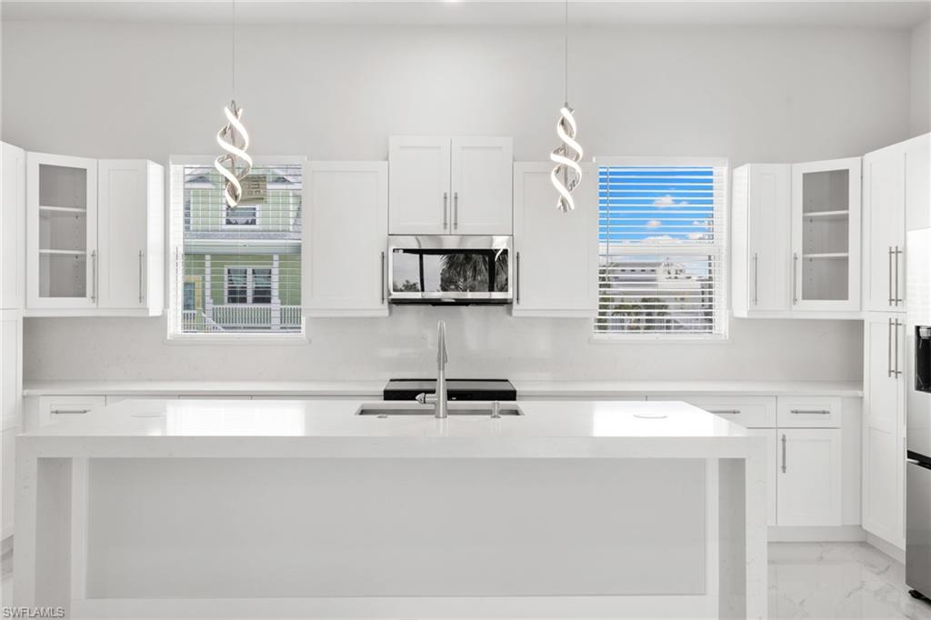 Kitchen featuring glass fronted cabinets, light stone countertops, an island with sink, stainless steel appliances, and white cabinetry